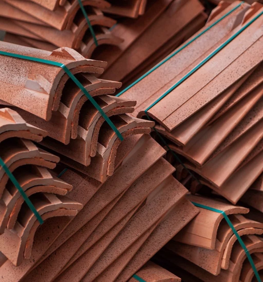 Stacks of reddish-brown roof tiles bundled together with green straps, ready for installation—just one example among the many types of roofs we repair.